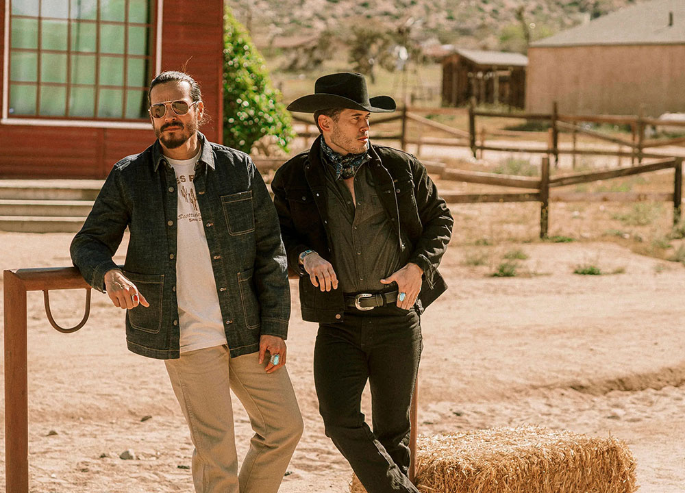 Two cowboys leaning against a fence